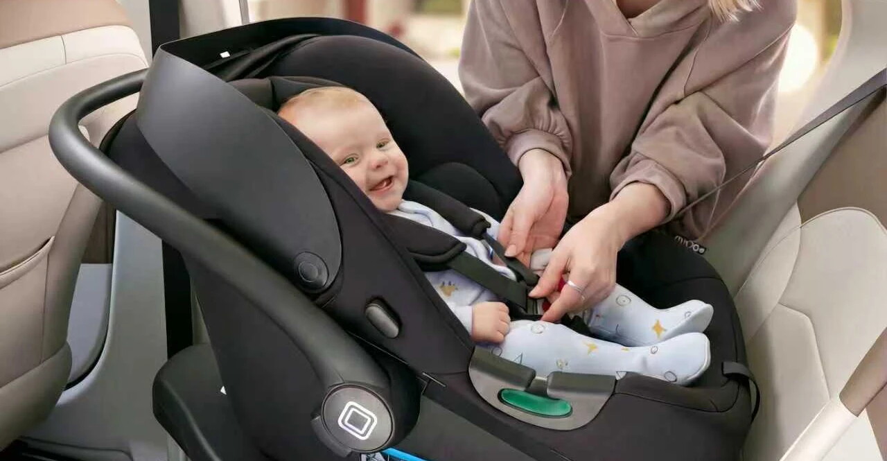 Mother buckling her baby into the MOON infant car seat LOLA on the 360° IQ Isofix base in the car